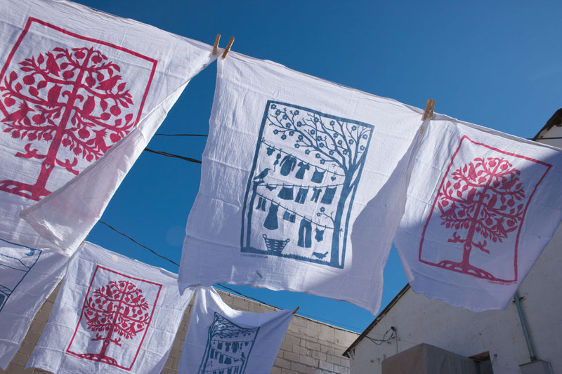 This photo has our Laundry Line and Tree of Life flour sack dish towels blwoing in the wind on a laundry line with the blue sky in the background.