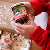 Person holding a jar of Heidis jam with a box of snacks in the background