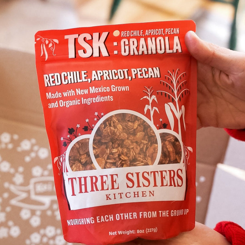 Red package of TSK Granola held by a person with a blurred indoor background