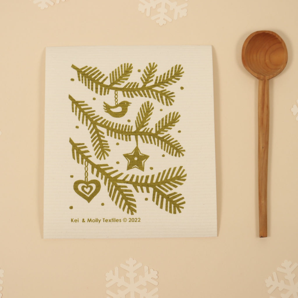  Kei & Molly Textiles Large Sponge Cloth “Pine branches!” design printed in Green propped with wooden spoon and snowflakes. 