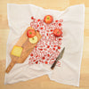 Kei & Molly "Apples & Pears" illustration: half pears and half apples printed in red on white cotton flour sack dish towel propped with wooden cutting board, cheese, knife and apples