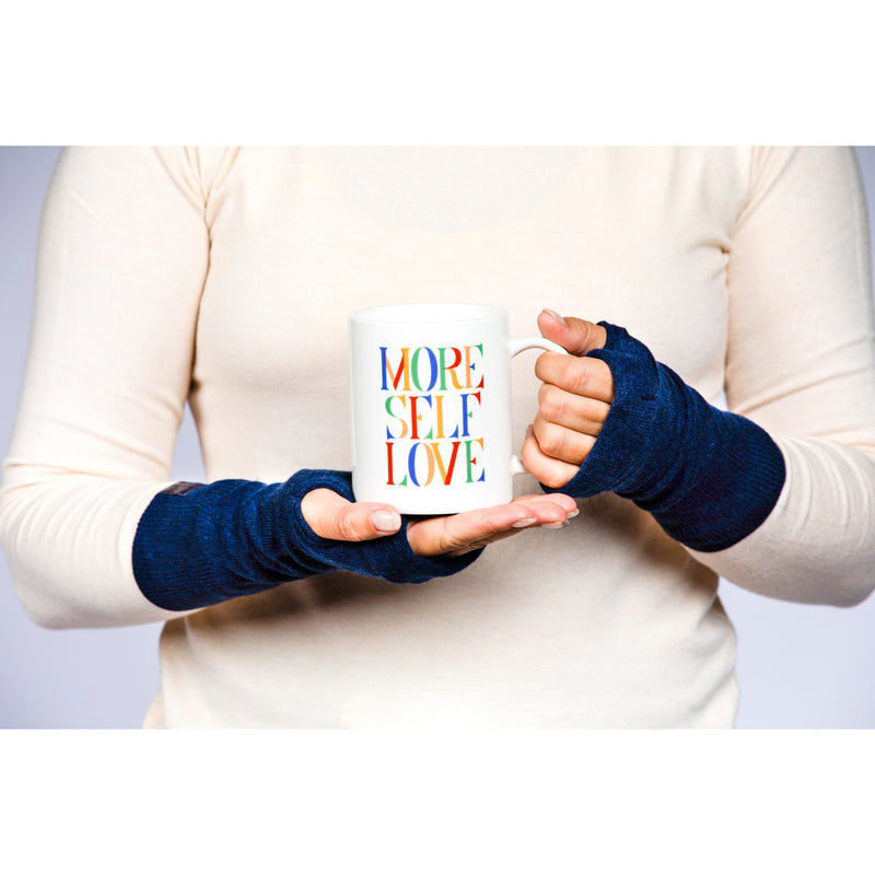 B. B Sheep cashmere fingerless gloves in denim blue. Model holding a mug.