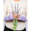B. B Sheep cashmere fingerless gloves in lilac. Model holding a lavender bouquet.